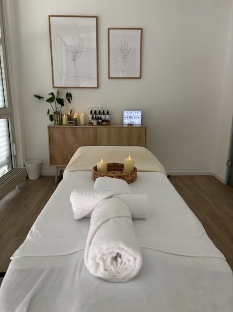 Massagebett mit weißen Handtüchern, Kerzen und dekorativen Elementen im Hintergrund.