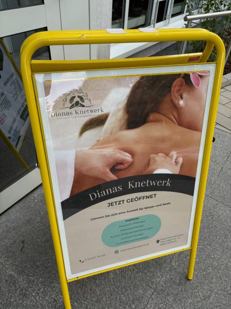 Werbeschild für Massageangebote mit einer sanften Hand auf dem Rücken einer Person.