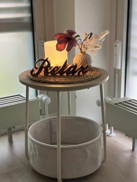 Holztisch mit der Aufschrift "Relax", einer Lampe und einer Blume in einer Vase.