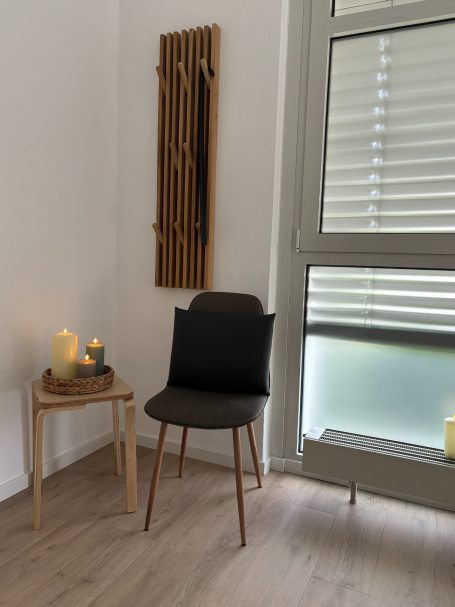 Ein Stuhl neben einem kleinen Tisch mit Kerzen, in einem hellen Raum mit Fenster.