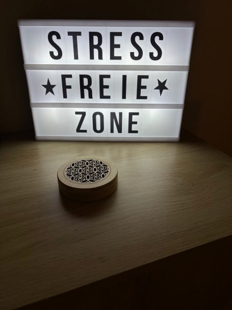 Leuchtschild mit dem Text "STRESSFREIE ZONE" über einem runden, perforierten Element.